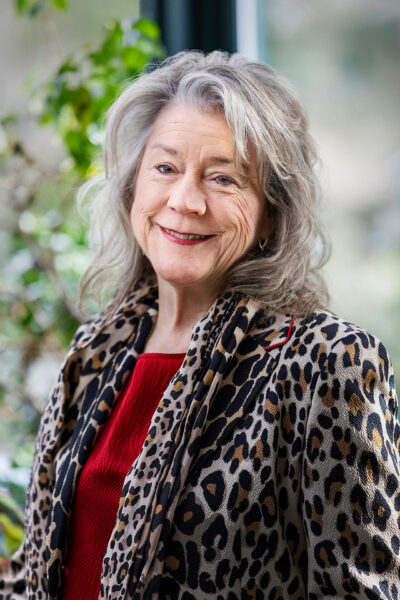 A photo of Carole Haas Gravagno smiling and wearing a animal-print blazer and red shirt.